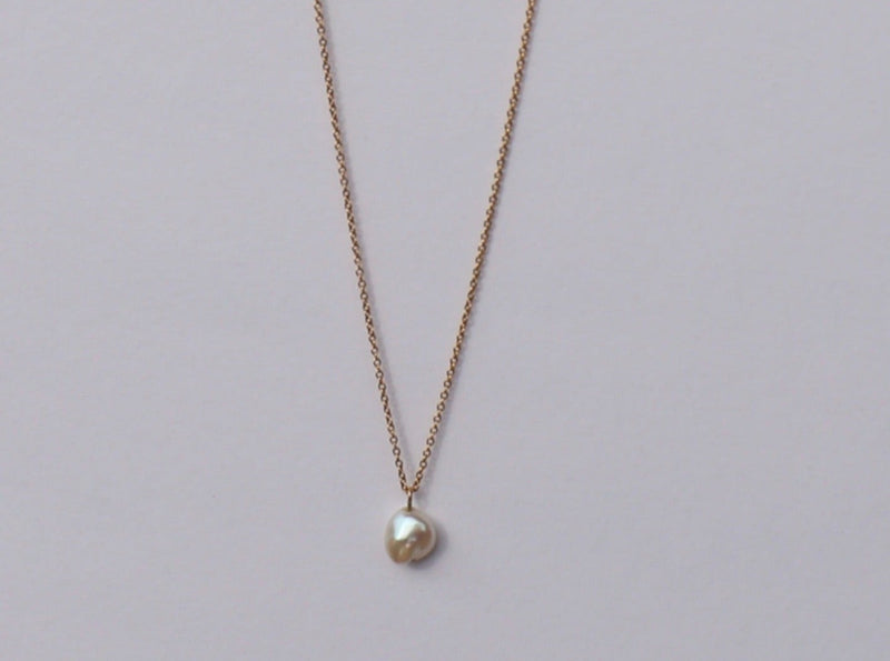 A gold-colored chain necklace with a Keshi pearl pendant, displayed against a neutral background.