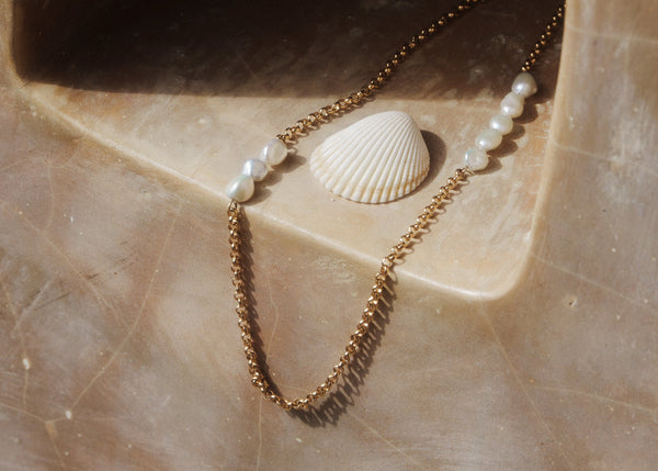 Aysha Chain - A gold-colored chain necklace with three keshi pearls attached, displayed on a textured background.