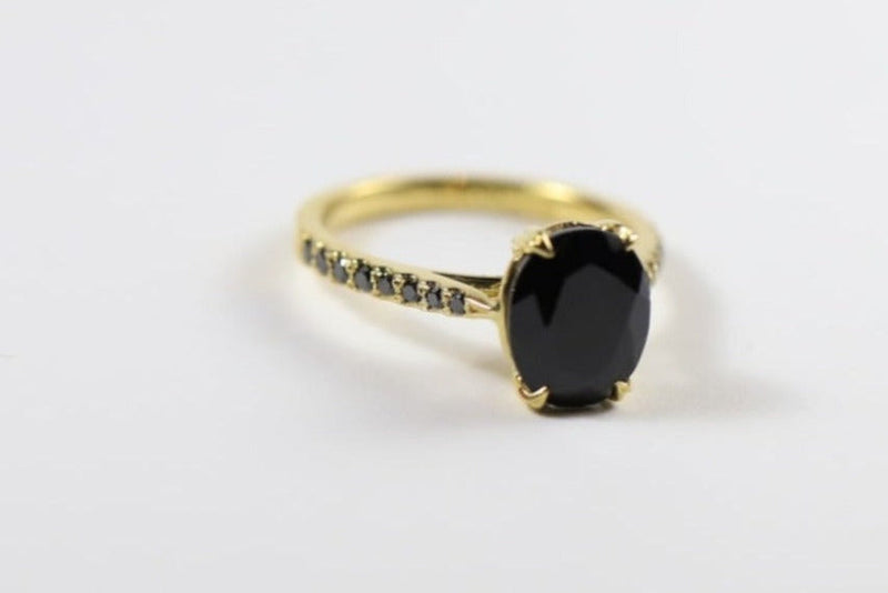 A 9ct gold ring with an oval black sapphire center stone and small black diamonds on the shoulders, set on a white background.