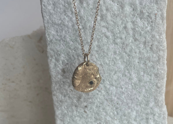 Gold necklace with a pendant on a textured stone surface
