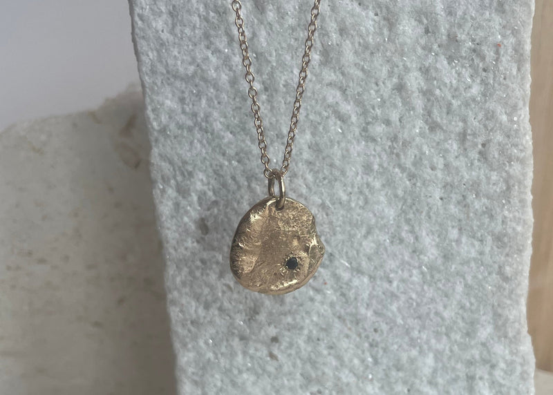 Gold necklace with a pendant on a textured stone surface
