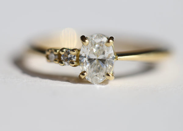 A gold ring featuring an oval central diamond with two smaller round diamonds on the side, set in a gold band.