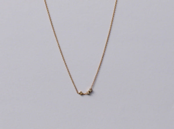 A delicate gold necklace with a round rose cut champagne diamond and two 2mm pearls set in claw settings, displayed against a light background.