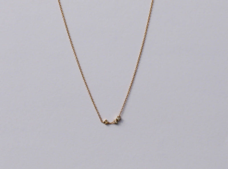 A delicate gold necklace with a round rose cut champagne diamond and two 2mm pearls set in claw settings, displayed against a light background.