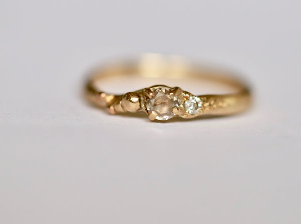 A gold band ring featuring a central rose cut champagne diamond flanked by a smaller diamond, with beading detail on the band.