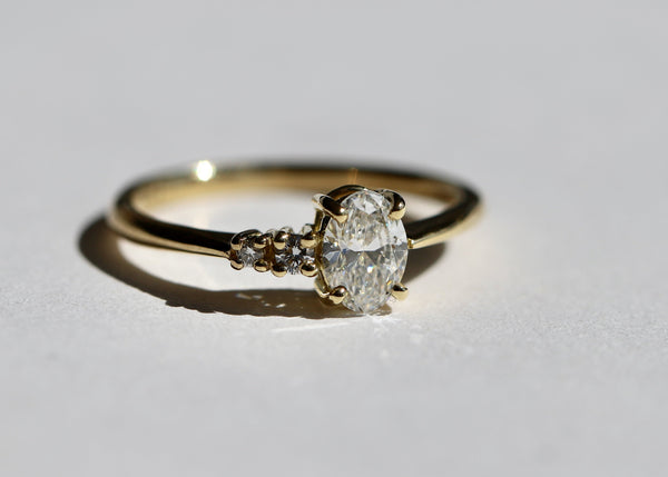 Gold ring with an oval diamond, fine band with two small round diamonds set in claw settings, on a light gray background