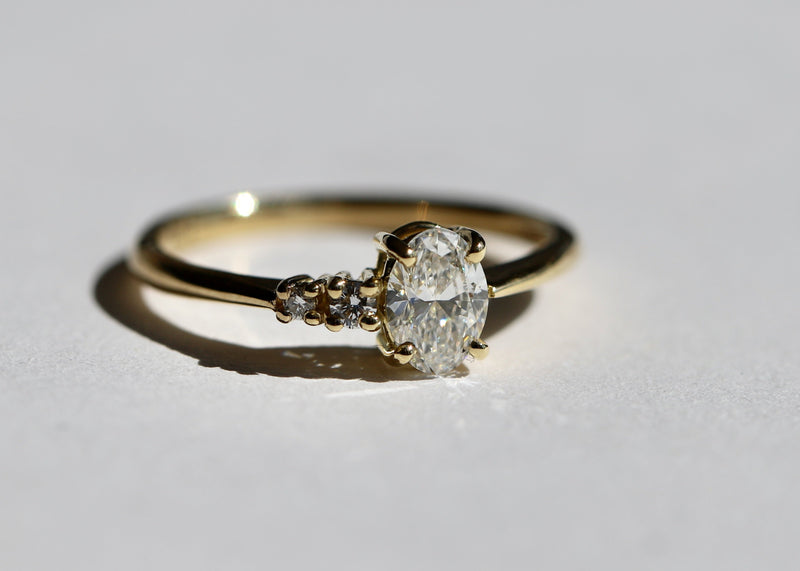 Gold ring with an oval diamond, fine band with two small round diamonds set in claw settings, on a light gray background