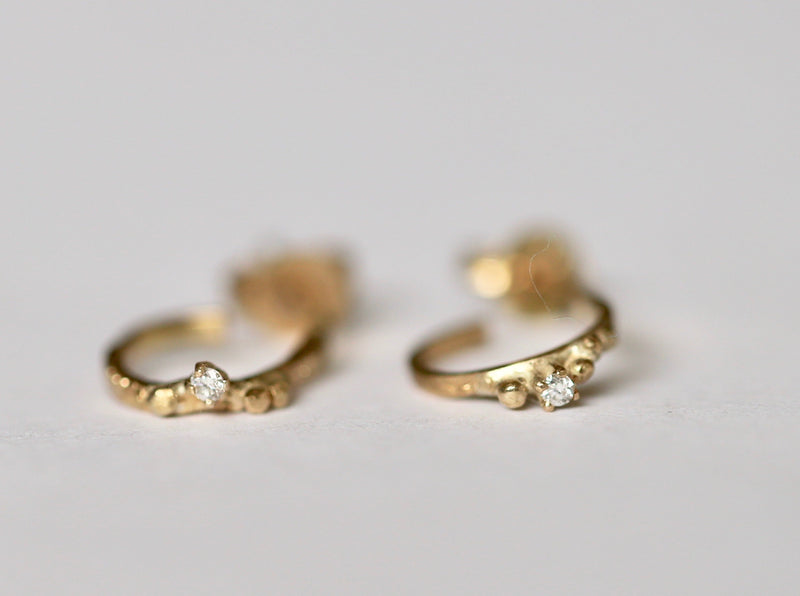 A pair of gold hoop earrings with a diamond and beading detail, designed to hugs the earlobe.
