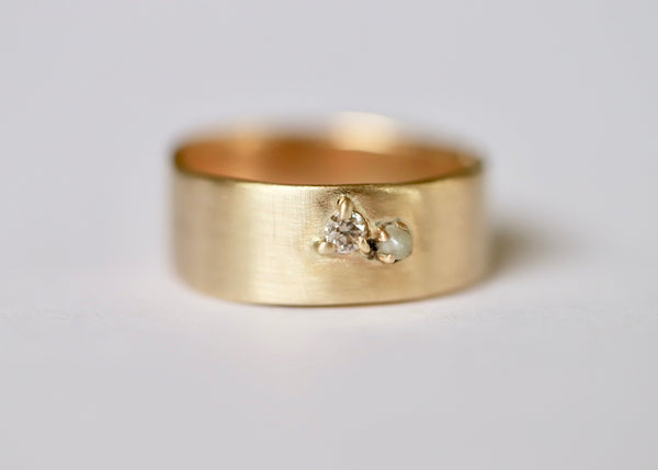 A gold cuff ring with an organic shape featuring a champagne diamond and a pearl set in the middle.