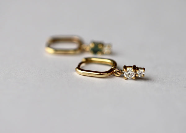 A pair of gold huggie-style earrings, one side features a round sapphire and a diamond, and the other side has a diamond duo.