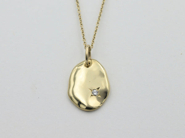 A gold pendant with an organic oval shape featuring a small round diamond set on one side, attached to a fine chain.