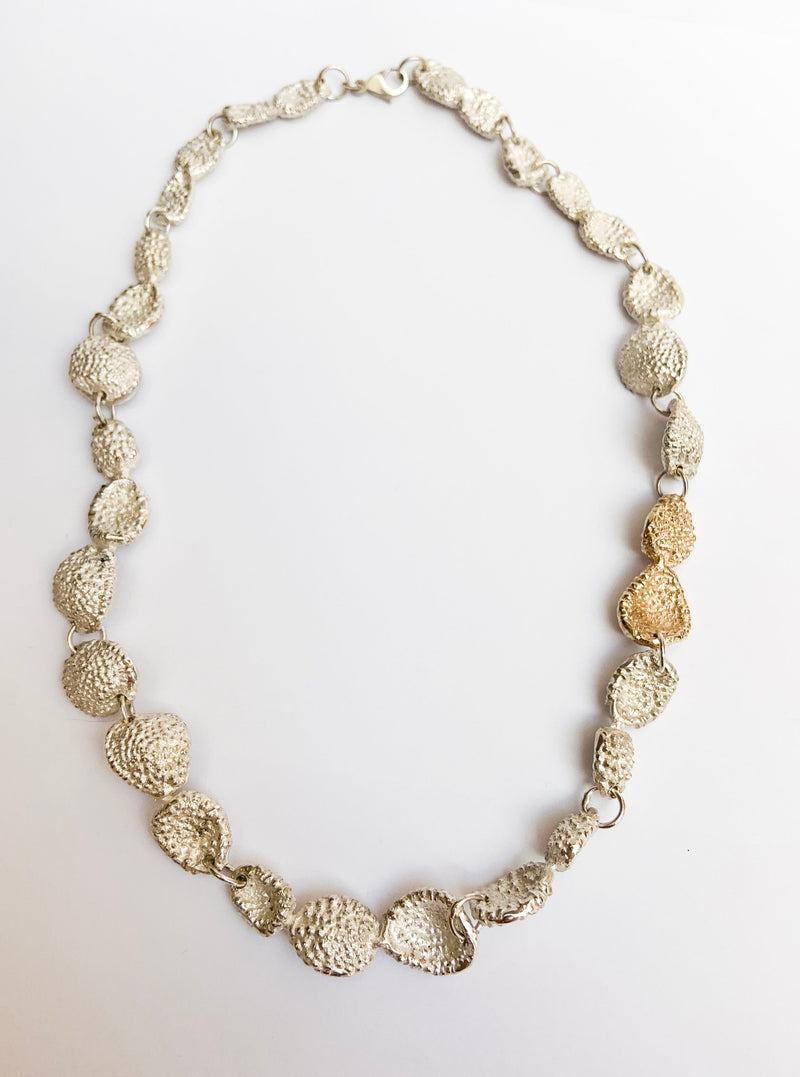 A silver choker-style necklace with a seaweed pattern, reminiscent of the ocean, laid out on a plain background.